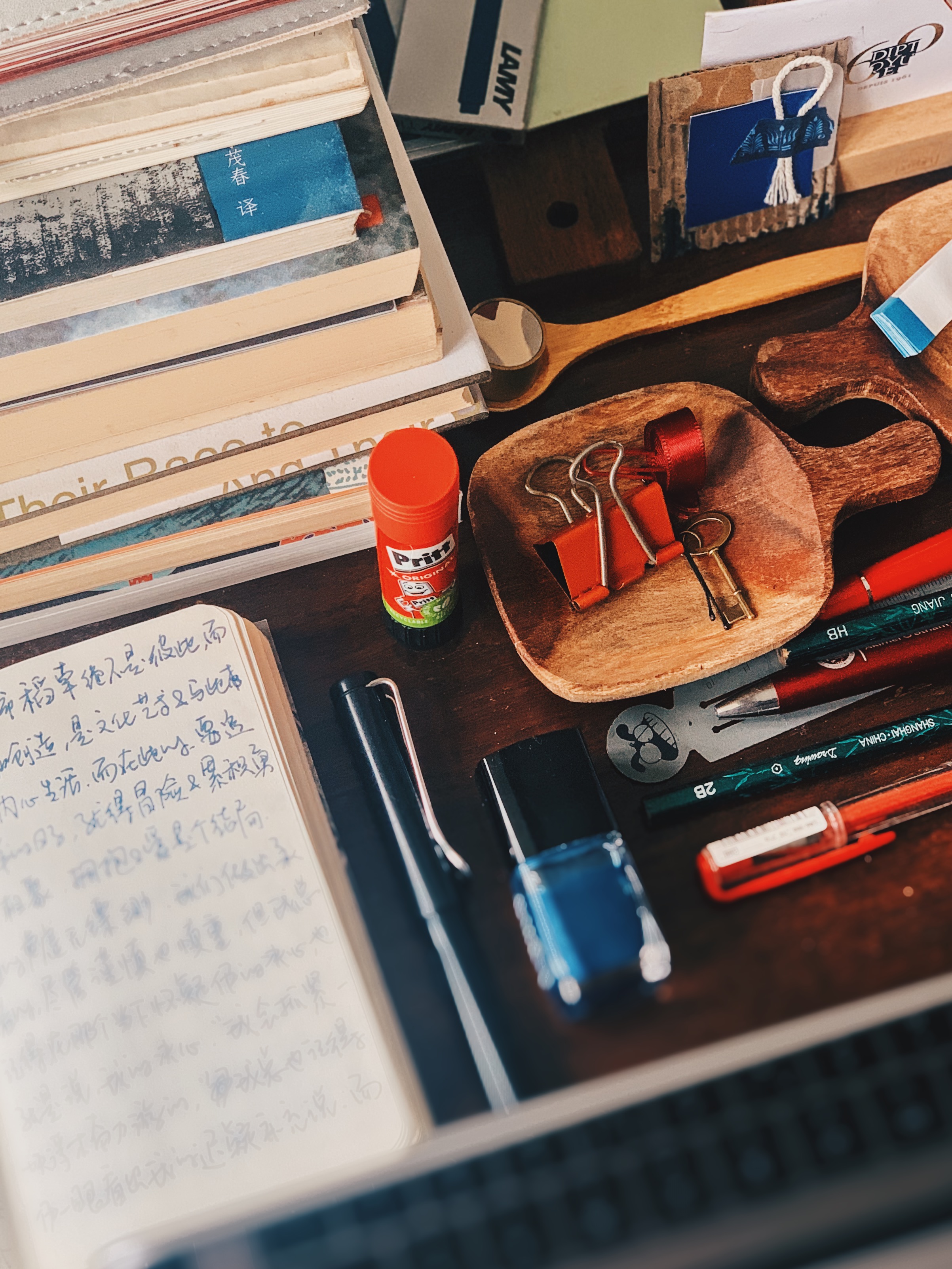 A writer's desk with notebooks, pens, books and small wooden objects.